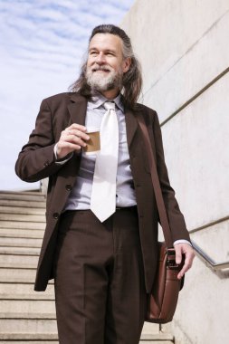 Şık takım elbiseli, şık bir iş adamı. Evrak çantası ve paket kahve ile şehirde şehir merdivenlerinden iniyor. İş ve orta yaşlı adam yaşam tarzı kavramı.
