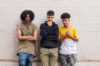 Beyaz tuğladan duvara yaslanan üç çok ırklı genç arkadaş, gençlik ve kentsel yaşam tarzında arkadaşlık kavramı