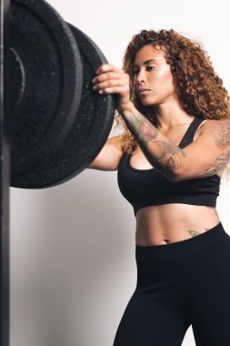 Spor salonunda spor yaparken ayakta duran ve halterlere ağırlık koyan kıvırcık saçlı güçlü sporcu spor salonu, spor konsepti ve aktif yaşam tarzı.