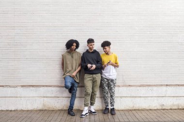 Beyaz tuğla duvara yaslanan üç etnik gruptan oluşan tam vücut, gençlik ve kentsel yaşam tarzında arkadaşlık kavramı, metin için kopyalanma alanı