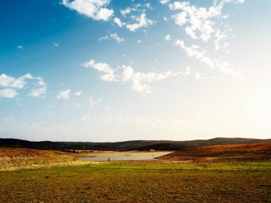 Ortasında bir göl olan geniş açık alan, gökyüzü açık ve mavidir, az sayıda bulut dağılmış, geniş bir arazide huzurlu ve huzurlu manzara kavramı, metin için kopyalanmış alan