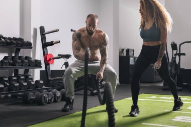 Spor salonundaki kadın eğitmenle egzersiz yaparken halatla egzersiz yapan kaslı sporcu, fitness konsepti ve aktif yaşam tarzı.