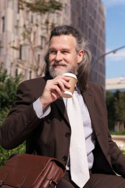 Şık kıyafetler içinde, şehir meydanında oturmuş bir fincan kahve içen, iş ve orta yaşlı adam yaşam tarzı kavramını benimseyen mutlu, olgun bir erkek.
