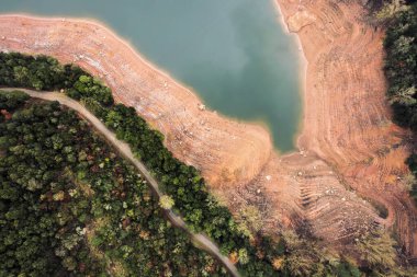 Ormanın yanındaki yarısı boş bir rezervuarın kıyı manzarası, insansız hava aracı manzarası, doğal arka plan.