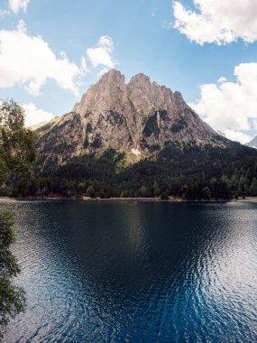 Büyük yeşil dağlar ve kozalaklı ağaçlarla çevrili sakin göl manzarası Aiguestortes I Estany of Saint Maurici Ulusal Parkı