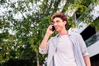 Genç adam mutlu bir şekilde caddede yürürken iyi bir ruh hali içinde cep telefonuyla konuşma, iletişim teknolojisi ve şehir yaşam tarzı kavramı, metin için metin metni paylaşımı
