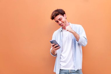 Genç adam cep telefonu tutuyor ve kutlama yaparken mutlu gülümsüyor, teknolojinin pozitif olması ve eğlenmesi kavramı, metin için telif alanı