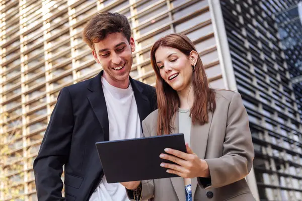 Erkek ve kadın mutlu bir şekilde gülümseyen dijital tablet ofis binasının önünde, erkek takım elbise giyiyor ve kadın ceket giyiyor, iş ve teknoloji kavramı.