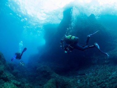 Üç dalgıçtan oluşan bir grup kristal berrak suda dalıyor güneş deniz yüzeyine yansıyor, eğlence amaçlı tüple dalış ve sualtı macerası kavramı