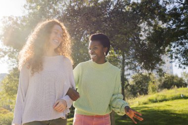 Parkta yürürken gülümseyen ve konuşan iki genç kadın. Arkadaşlık ve arkadaşlık kavramı. Birlikte vakit geçirmenin zevki.