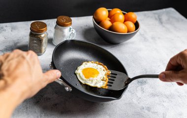 Klasik bir kahvaltı titreşimi için, bir spatula, bir kase yumurta ve tuzluk ile çevrili, yapış yapış olmayan bir yüzey üzerinde güneşli bir yumurta..