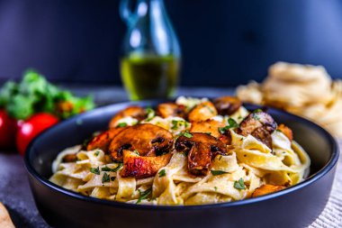 Üzerine altın tavuk ve sotelenmiş maydanozla süslenmiş lezzetli bir kremalı tagliatelle makarnası. Kırsal bir arka planda siyah bir kasede sunuldu..