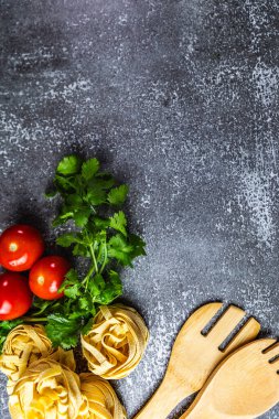 Taze kişniş, olgun kırmızı domatesler ve ahşap çatal bıçaklar ile dokuma kaplı, düzgün düzenlenmiş tagliatelle makarna yuvaları içeren, sade, düz bir kompozisyon..