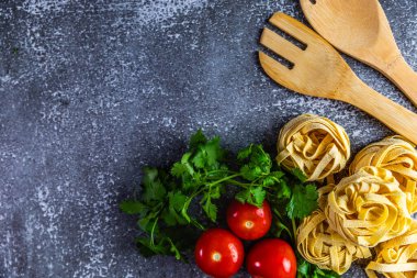 Taze kişniş, olgun kırmızı domatesler ve ahşap çatal bıçaklar ile dokuma kaplı, düzgün düzenlenmiş tagliatelle makarna yuvaları içeren, sade, düz bir kompozisyon..
