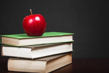 Bir yığın kitabın üzerinde kırmızı elma. Masada bir yığın ders kitabı var. Kitap okuyorum. Yüksek kalite fotoğraf