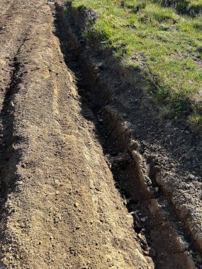 Güneş ışığı altında çimenli bir arazide yeni kazılmış bir çukur. Çeşitli yaratıcı ihtiyaçlar için uygun
