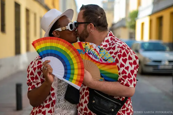 stock image Gay couple with a hand fan with the colors of the LGTBI flag