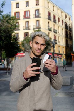 Yakın plan genç, mutlu ve zarif bir adam, sokakta yürüyor, cep telefonu ve kredi kartıyla online alışveriş yapıyor..