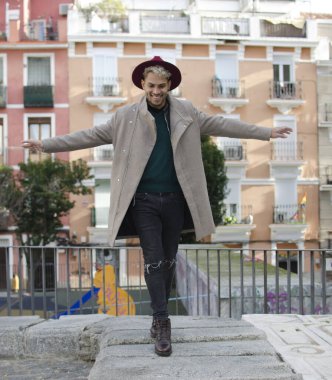 Gri ceketli, kırmızı şapkalı, sokakta dengeyi sağlayan genç bir model.