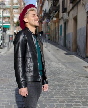 Deri ceketli, kırmızı şapkalı, sokakta gülümseyen genç bir manken.