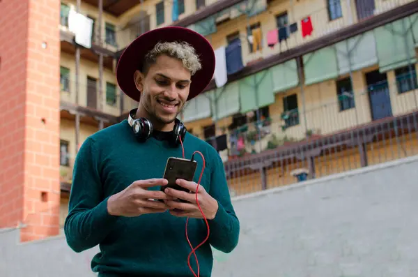 Kulaklıklı genç adam akıllı telefonu elinde tutuyor ve şehirde müzik dinliyor.