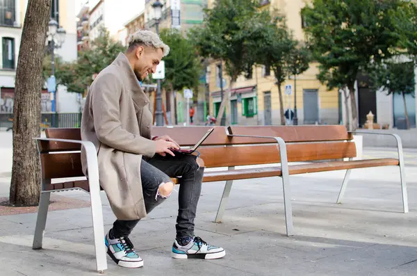 Yakın plan genç, mutlu ve zarif bir adam sokakta dizüstü bilgisayarla çalışıyor.