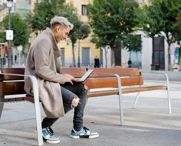 Yakın plan genç, mutlu ve zarif bir adam sokakta dizüstü bilgisayarla çalışıyor.