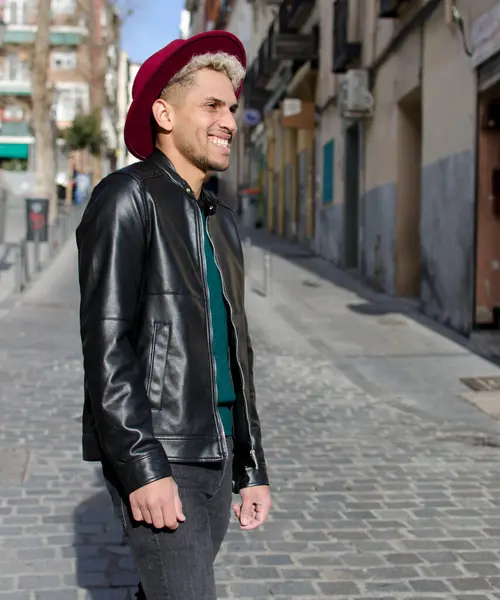 Deri ceketli, kırmızı şapkalı, sokakta gülümseyen genç bir manken.