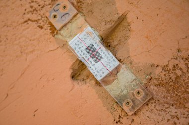 Deep crack in a damaged old plaster wall with plastic mechanical crack meter designed to measure movement across surface cracks and joints