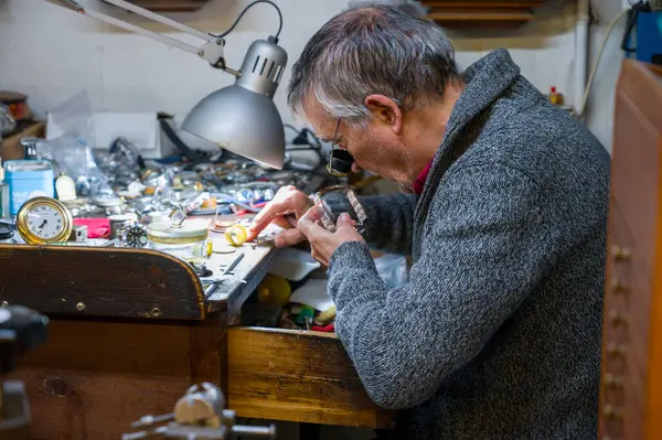 Madrid, İspanya. 21 Mart 2025. Erkek saat tamircisi tamir atölyesindeki kol saati takımlarını tamir ediyor.