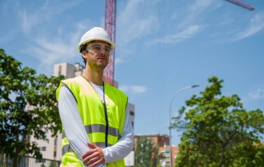 Güvenlik kaskı ve yansıtıcı yeleği olan profesyonel erkek inşaat işçisi. İnşaat alanında arka planda inşaat çalışması var.