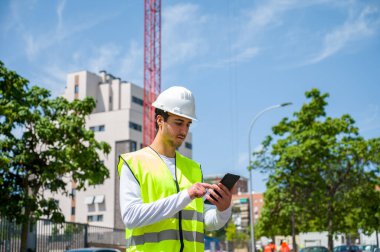 Güvenlik kaskı ve yansıtıcı yeleği olan profesyonel erkek inşaat işçisi. İnşaat alanında arka planda inşaat çalışması var.