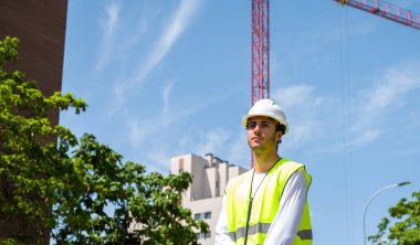 Güvenlik kaskı ve yansıtıcı yeleği olan profesyonel erkek inşaat işçisi. İnşaat alanında arka planda inşaat çalışması var.