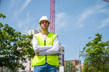 Güvenlik kaskı ve yansıtıcı yeleği olan profesyonel erkek inşaat işçisi. İnşaat alanında arka planda inşaat çalışması var.