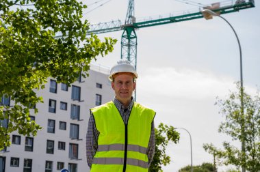 İnşaat alanında güvenlik kaskı ve yansıtıcı yeleği olan profesyonel bir inşaat işçisi.