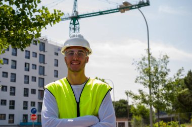 Güvenlik miğferi ve yansıtıcı yeleği olan profesyonel inşaat işçisi. İnşaat alanında güvenle gülümsüyor.