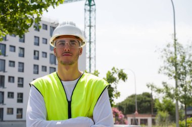 Güvenlik kaskı ve yansıtıcı yeleği olan profesyonel erkek inşaat işçisi. İnşaat alanında arka planda inşaat çalışması var.