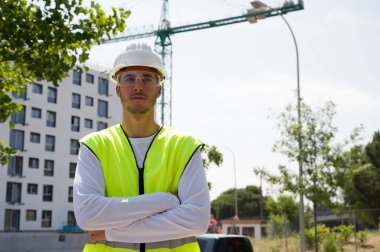 Güvenlik kaskı ve yansıtıcı yeleği olan profesyonel erkek inşaat işçisi. İnşaat alanında arka planda inşaat çalışması var.