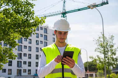 Güvenlik kaskı ve yansıtıcı yeleği olan profesyonel erkek inşaat işçisi. İnşaat alanında arka planda inşaat çalışması var.