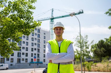 Güvenlik kaskı ve yansıtıcı yeleği olan profesyonel erkek inşaat işçisi. İnşaat alanında arka planda inşaat çalışması var.