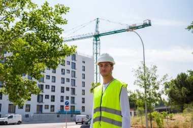 Güvenlik kaskı ve yansıtıcı yeleği olan profesyonel erkek inşaat işçisi. İnşaat alanında arka planda inşaat çalışması var.