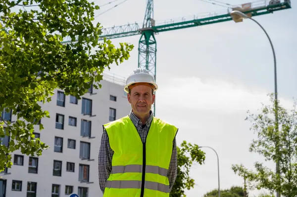 İnşaat alanında güvenlik kaskı ve yansıtıcı yeleği olan profesyonel bir inşaat işçisi.