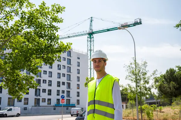 Güvenlik kaskı ve yansıtıcı yeleği olan profesyonel erkek inşaat işçisi. İnşaat alanında arka planda inşaat çalışması var.