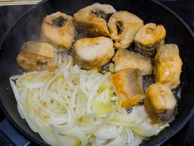 Kızarmış Habbsi hake ya da kızartma sırasında tavada soğanlı Arjantin hake..