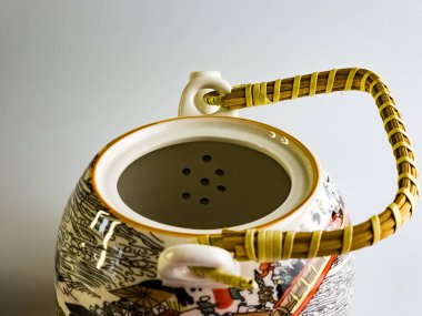 Yakın plan. Soyut desenli seramik çaydanlık ve beyaz arkaplanda hasır saman sapı.