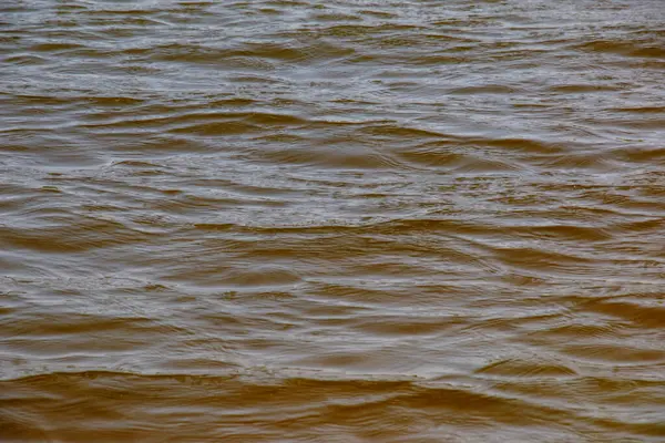 Dinyeper Nehri 'nin dalgalı su yüzeyinin arka planı. Sonbaharda batan güneşin ışınlarında nehir suyu. Nehir suyunun doğal rengi. Küçük dalgalı su.