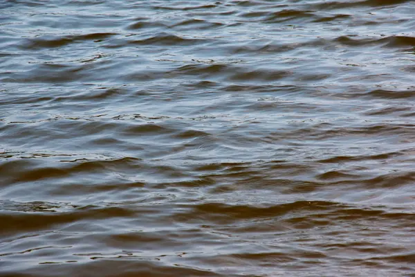 Dinyeper Nehri 'nin dalgalı su yüzeyinin arka planı. Sonbaharda batan güneşin ışınlarında nehir suyu. Nehir suyunun doğal rengi. Küçük dalgalı su.