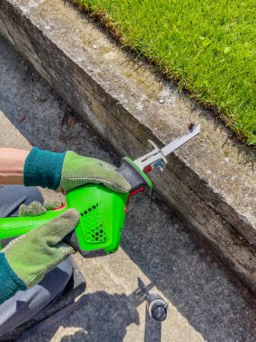 Eldivenli erkek eller beton kirişten çıkan metal cıvataları elektrikli testereyle kesiyor..