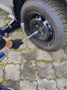 Nitra, Slovakya - 08.05.2025: araba servisi. Tekerlek değiştirme. Mevsimlik lastik değişimi. Tamirci tekerleği iki eliyle ve anahtarla çıkarır..