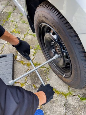 Nitra, Slovakya - 08.05.2025: araba tamiri. Tekerlek değiştirme. Mevsimlik lastik değişimi. Tamirci tekerleği iki eliyle ve İngiliz anahtarıyla çıkarıyor..